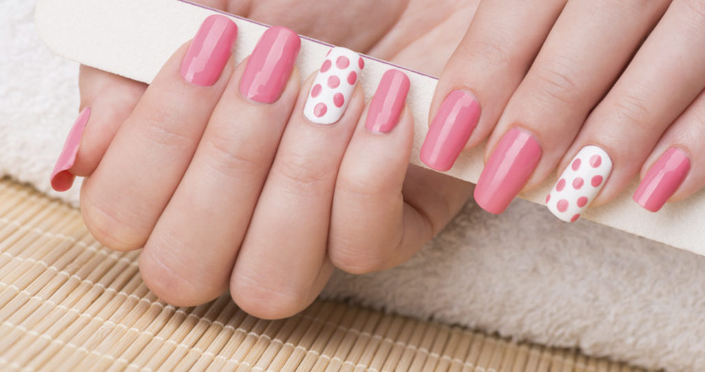 Beauty treatment photo of nice manicured woman fingernails holding nail file. Feminine nail art with nice pink and white nail polish.